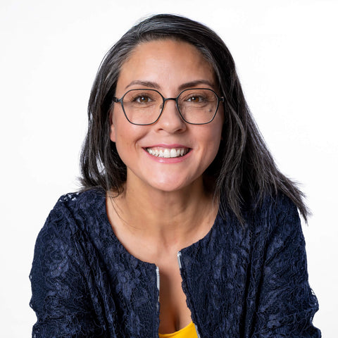 Alexandra Gölz frontal bis zur Brust. Trägt Brille, blauen Blaser, gelbes Oberteil. Lächelt.