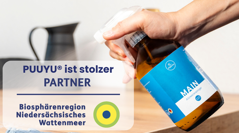 Hand mit PUUYU® MAIN Allzweckreiniger; daneben der Hinweis: PUUYU® ist stolzer Partner der Biosphärenregion Niedersächsisches Wattenmeer.